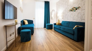 A modern living room with two blue sofas, a round ottoman, a flat-screen TV, and a patterned wall. - Atmosfere Guest House - 5 Terre e La Spezia (La Spezia)