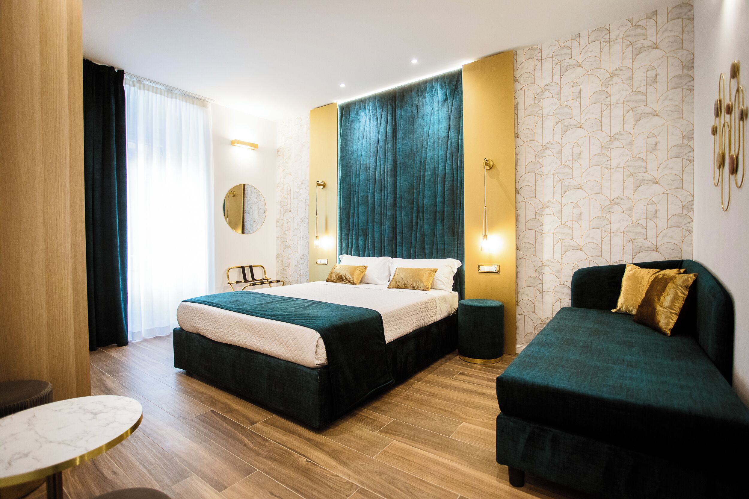 Una habitación de hotel moderna con una cama grande, un sofá más pequeño, una mesa redonda y vistas a la ciudad.