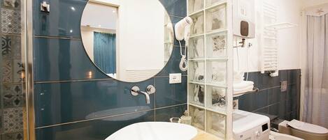 Un baño moderno con un espejo redondo, un lavamanos blanco, una ducha con mampara de vidrio y una lavadora.