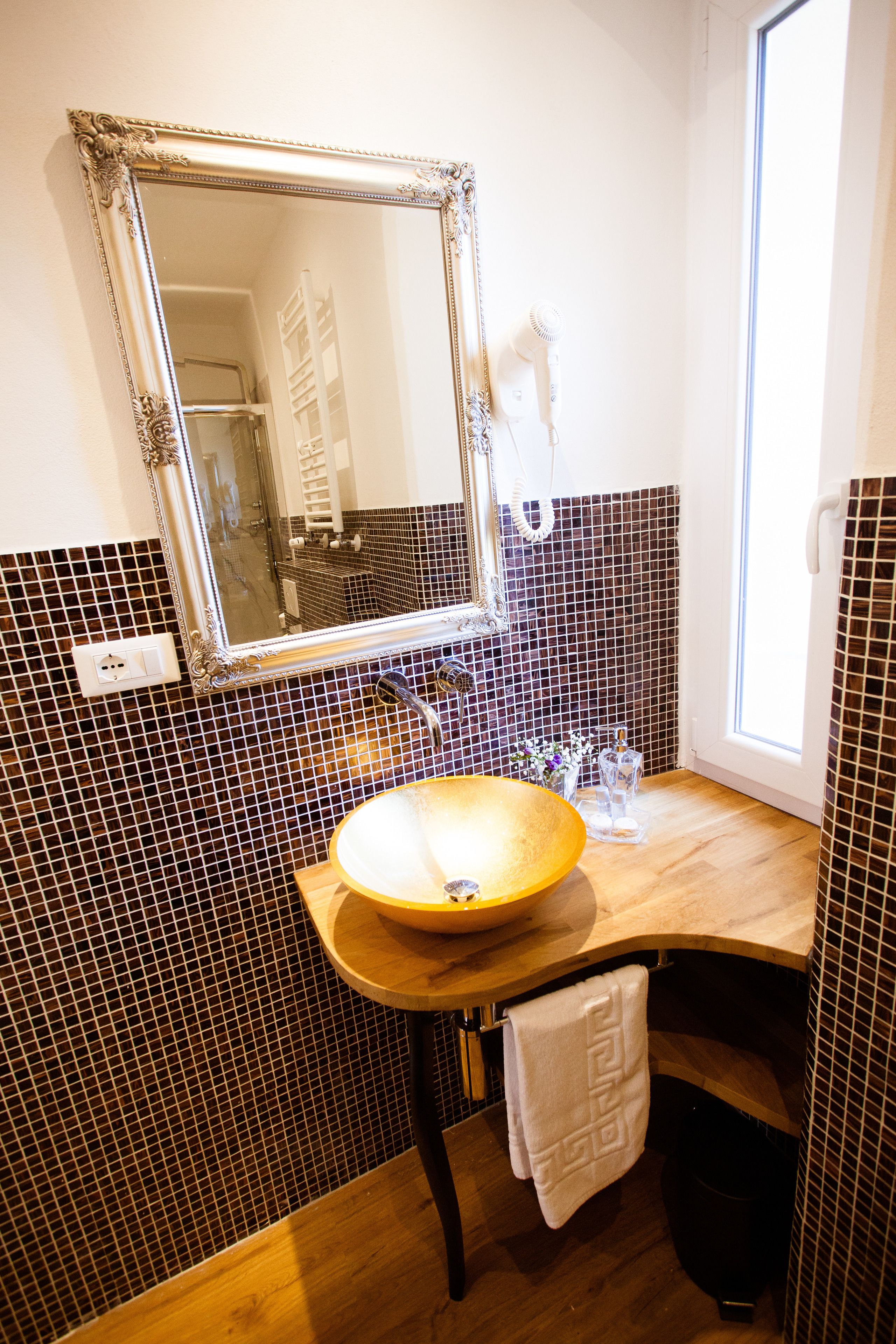 A bathroom with a large mirror, a wooden vanity, a sink, and a towel hanging on the wall.