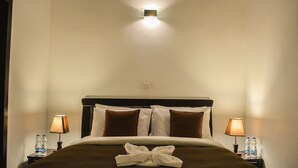 A neatly made bed with a brown blanket, two pillows, and a folded towel on the bed. There are two bedside tables with lamps and water bottles on them. - Panoramic Holiday Apartment Seagull Complex - Nuwara Eliya (Nuwara Eliya)