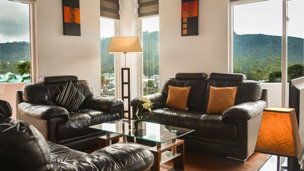 A modern living room with leather sofas, a glass coffee table, and a view of a mountainous landscape through large windows. - Panoramic Holiday Apartment Seagull Complex - Nuwara Eliya (Nuwara Eliya)