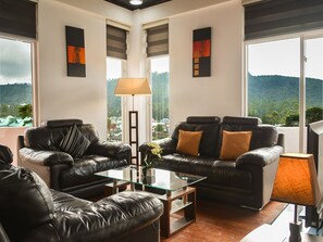 A modern living room with leather sofas, a glass coffee table, and a view of a mountainous landscape through large windows. - Panoramic Holiday Apartment Seagull Complex - Nuwara Eliya (Nuwara Eliya)