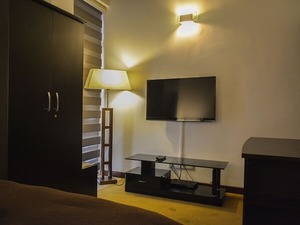 Habitación de hotel con televisión montada en la pared, un escritorio con lámpara y un armario.