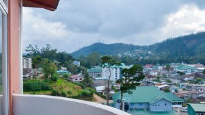 A view from a balcony overlooking a town with various buildings, including a prominent white building with a green roof, and a hillside in the background. - Panoramic Holiday Apartment Seagull Complex - Nuwara Eliya (Nuwara Eliya)