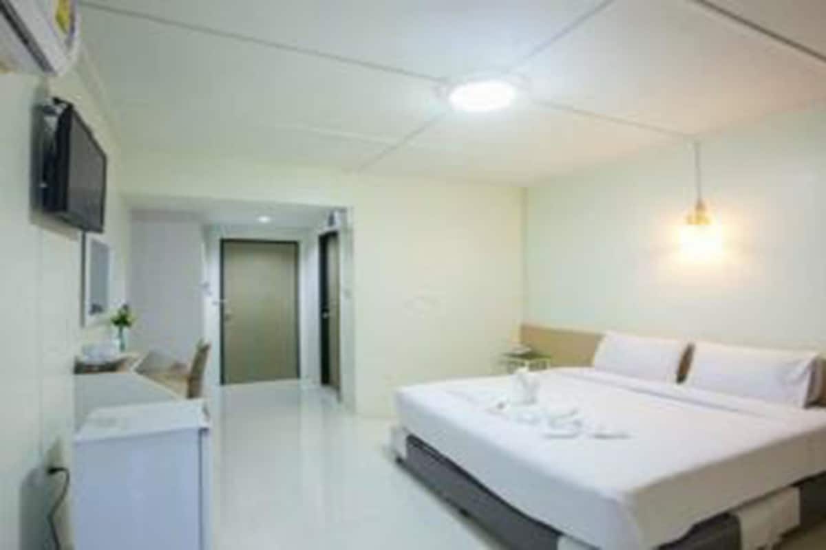 Una habitación de hotel con una cama, televisión y una pequeña mesa con un florero.