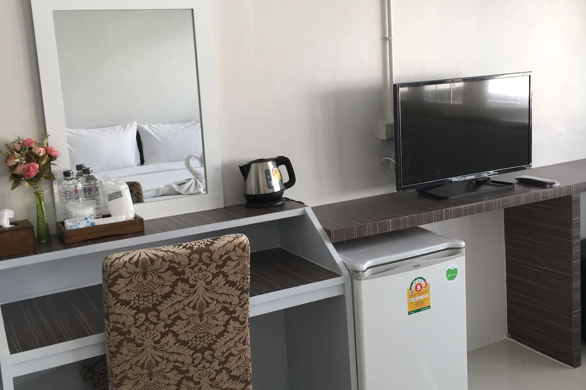 Habitación de hotel con cama, escritorio con silla, televisor, refrigerador y una pequeña kitchenette.