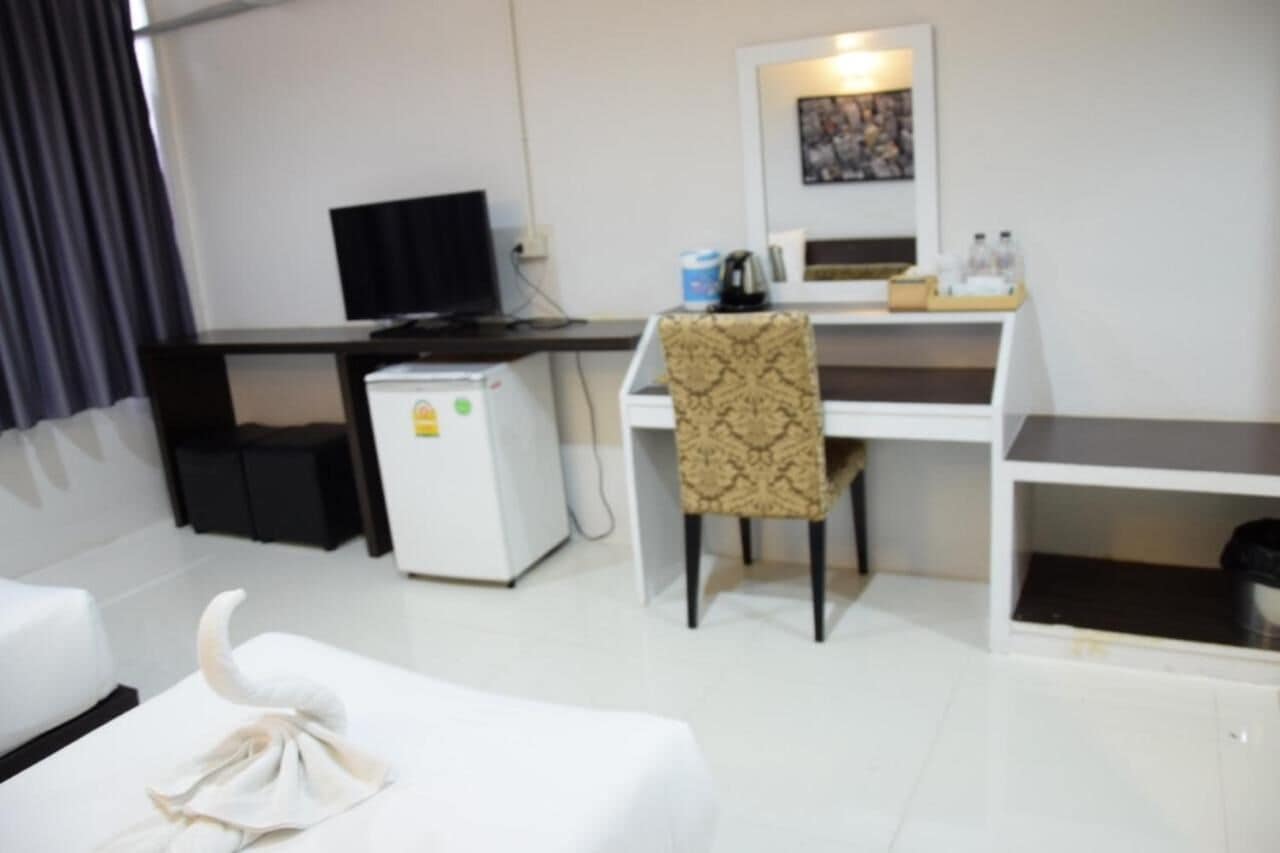 Een compacte hotelkamer met een wit bureau, een kleine koelkast, een televisie en een gestreept stoeltje.