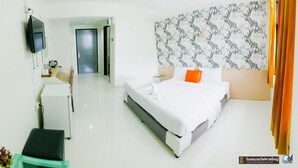 Quarto de hotel com cama, escrivaninha, cadeira, televisão e parede estampada.