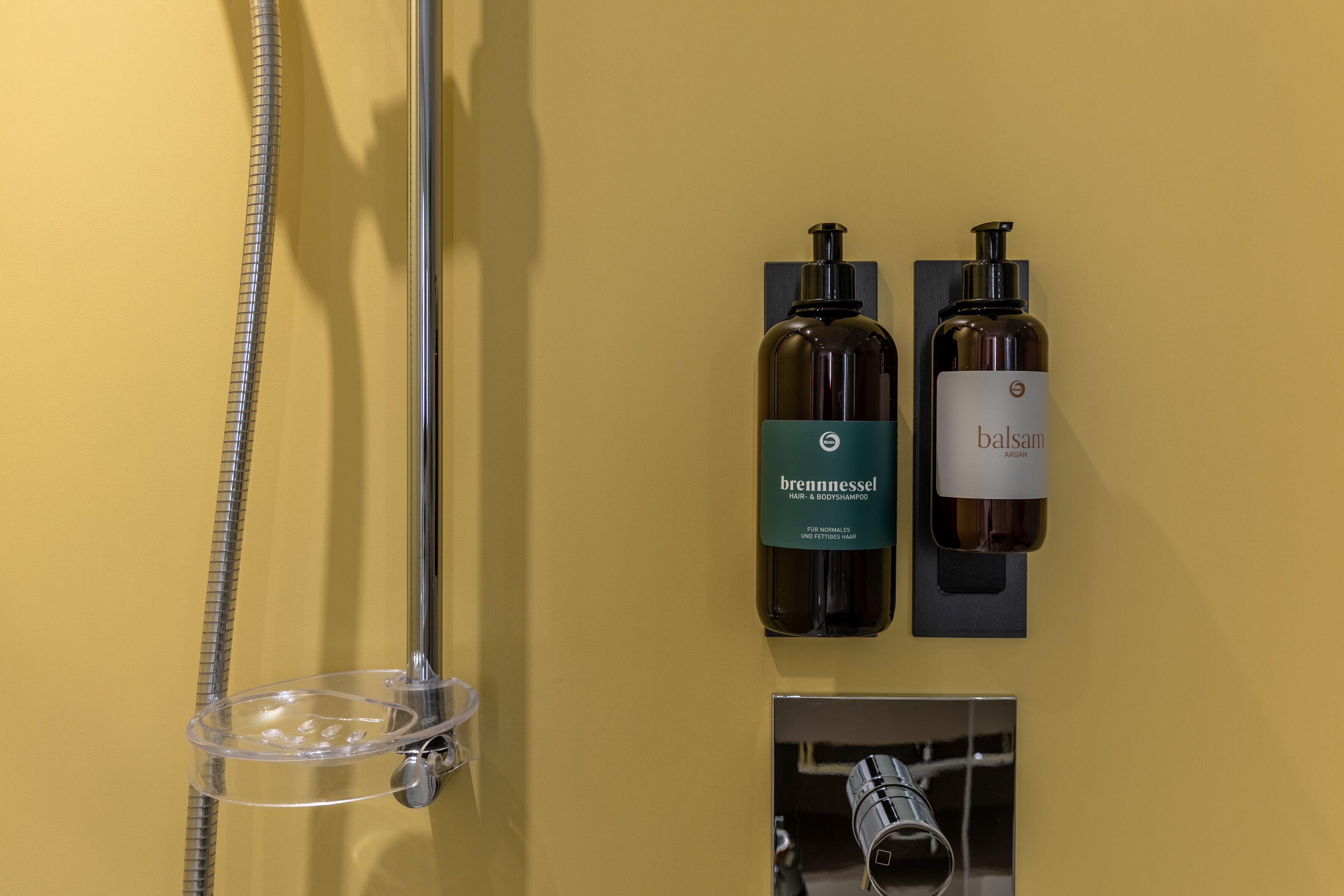 A bathroom with a shower, two bottles of hair and body shampoo, and a soap dispenser.