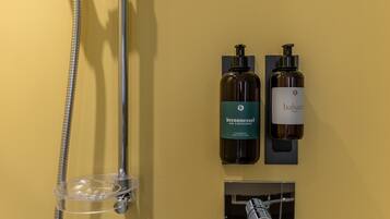 A bathroom with a shower, two bottles of hair and body shampoo, and a soap dispenser.