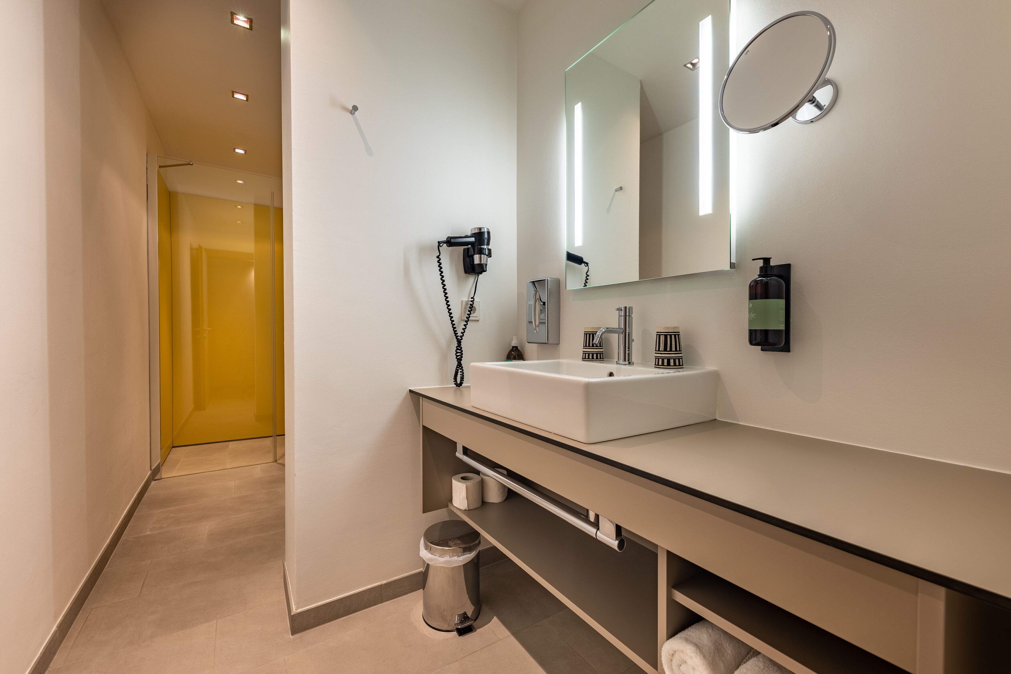A modern bathroom with a white sink, mirror, and a hairdryer mounted on the wall.