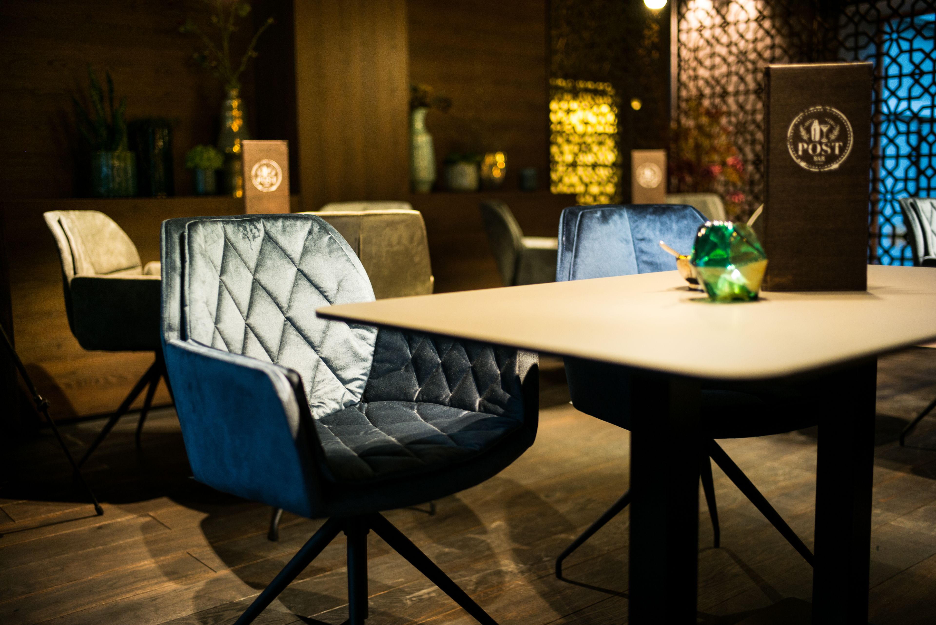 A modern dining area with a wooden table and chairs, a decorative vase, and a sign with the word "POST".