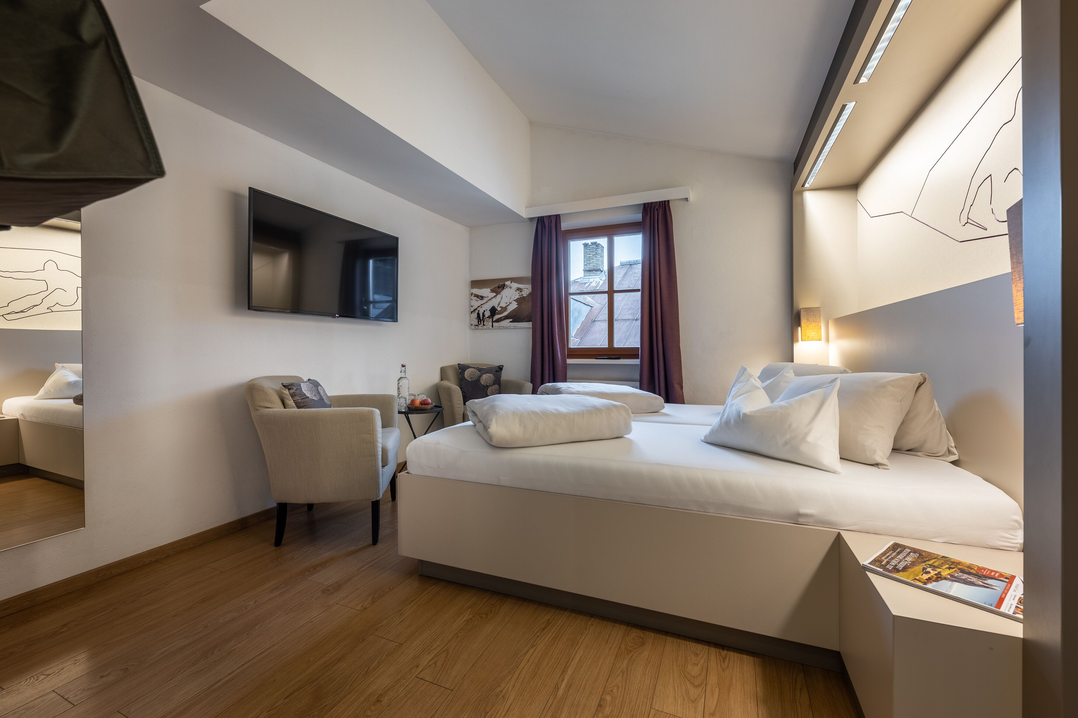 Una habitación de hotel moderna con una cama grande, un escritorio, una silla, un televisor de pantalla plana y un ventanal con cortinas.