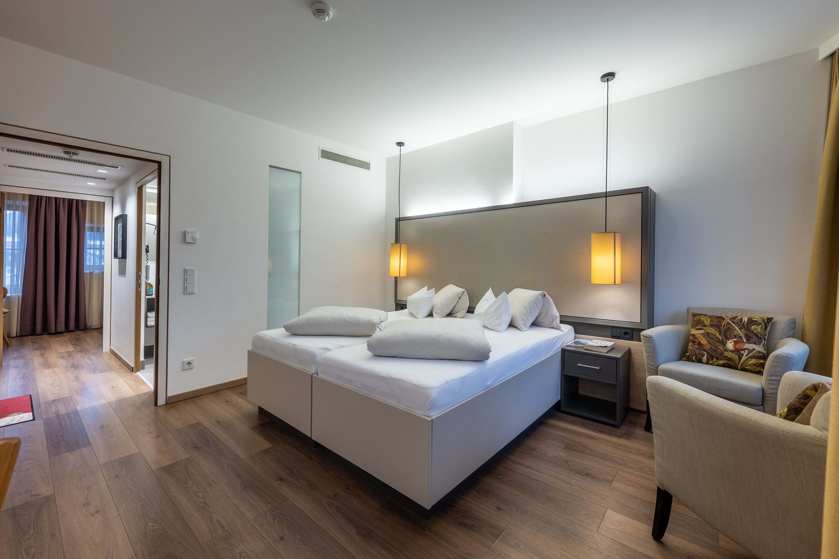 A modern hotel room with a large bed, bedside tables, a chair, and a large mirror.