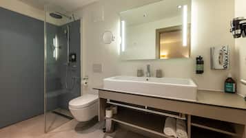 Un bagno moderno con cabina doccia in vetro, un lavandino bianco e uno specchio grande.
