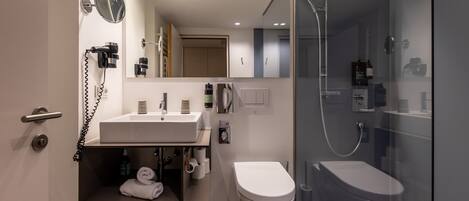 A modern bathroom with a glass-enclosed shower, a white toilet, and a vanity with a mirror and hairdryer.