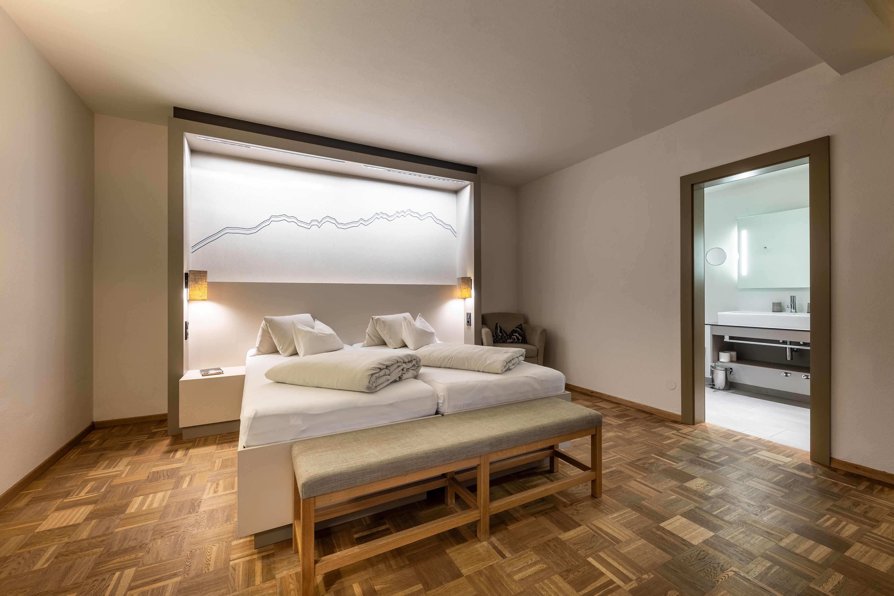 A modern bedroom with a bed, bench, bedside tables, and a wall-mounted light fixture.