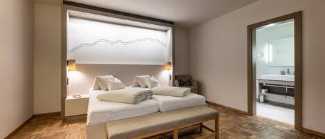 Un dormitorio moderno con cama, banco, mesitas de noche y una lámpara de pared.