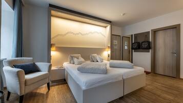 Quarto de hotel moderno com uma cama grande, área de estar com uma poltrona e uma obra de arte na parede.