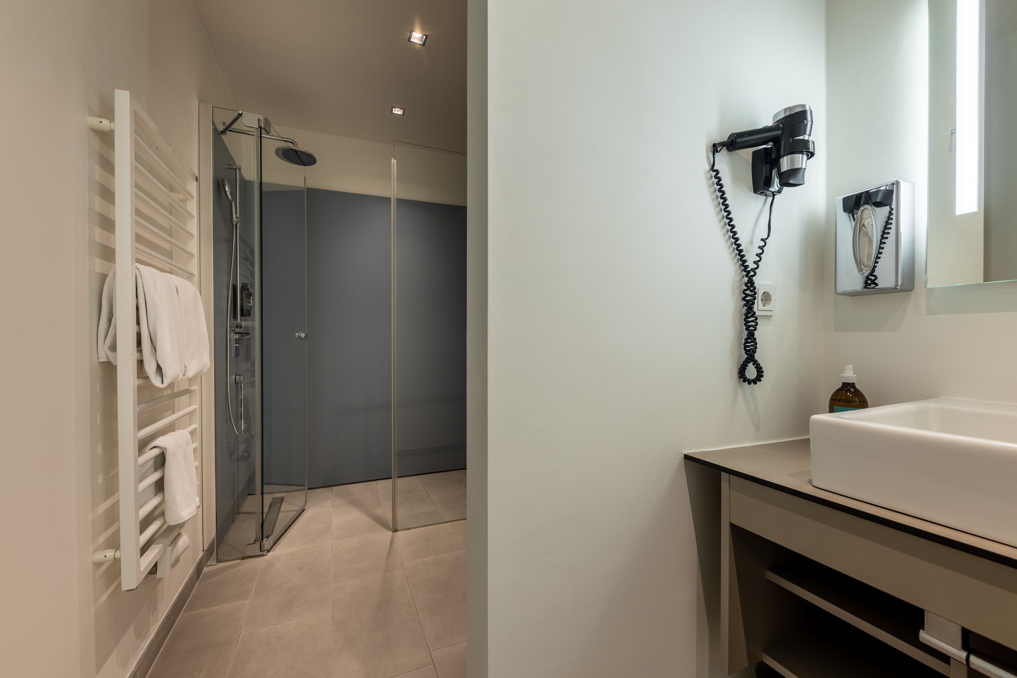 Un baño moderno con cabina de ducha de vidrio, un lavamanos blanco y un secador de pelo montado en la pared.