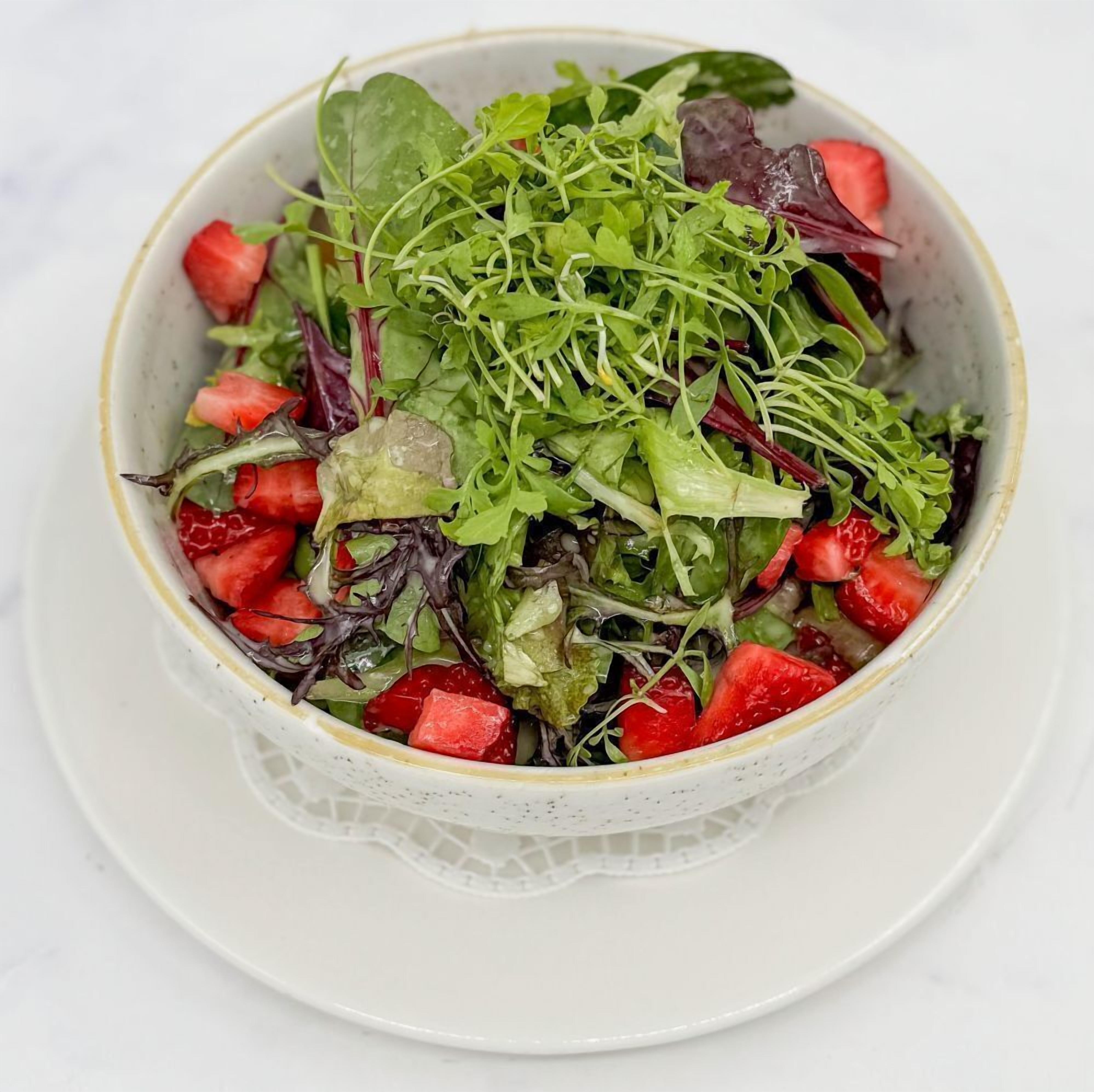 A bowl of salad with various greens and strawberries.