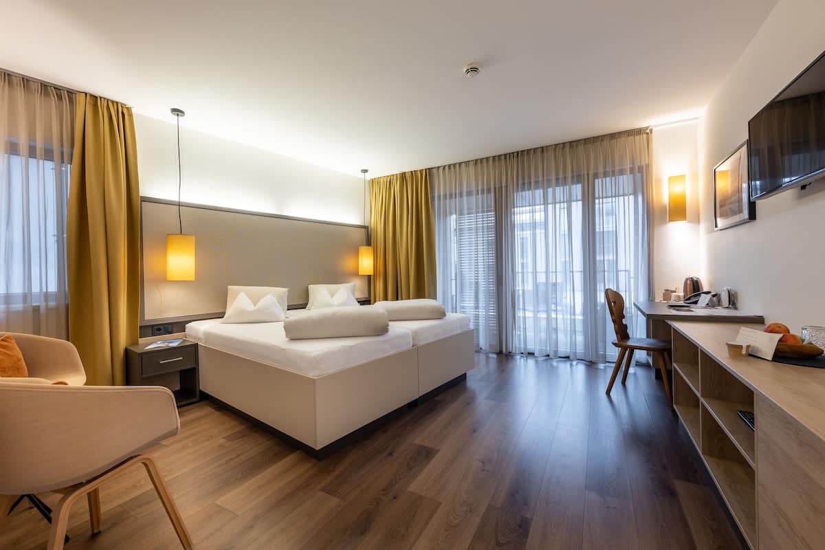 A modern hotel room with a large bed, a desk, a chair, and a TV.