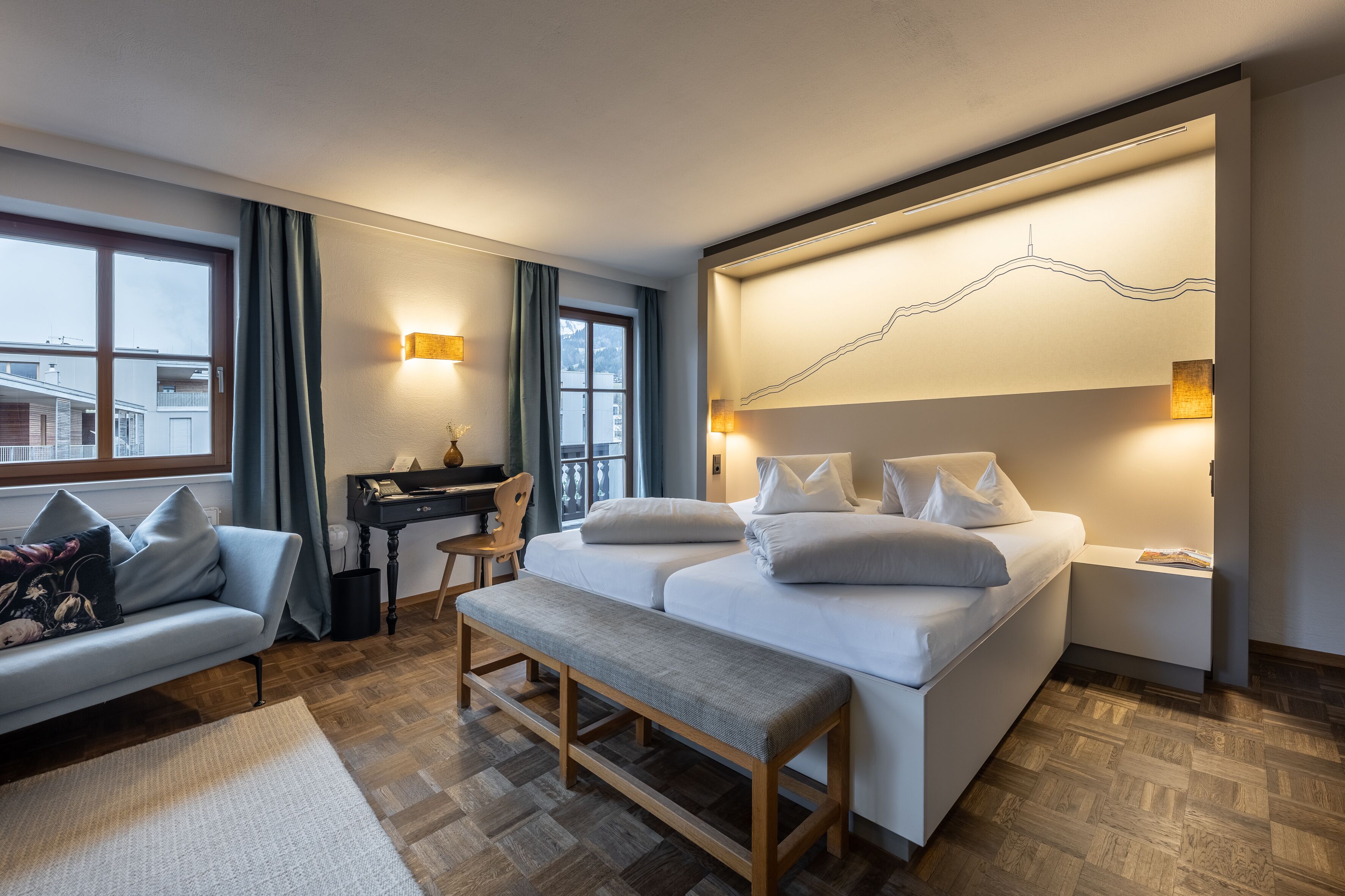 A modern hotel room with a large bed, a desk, a sofa, and a view of the city.