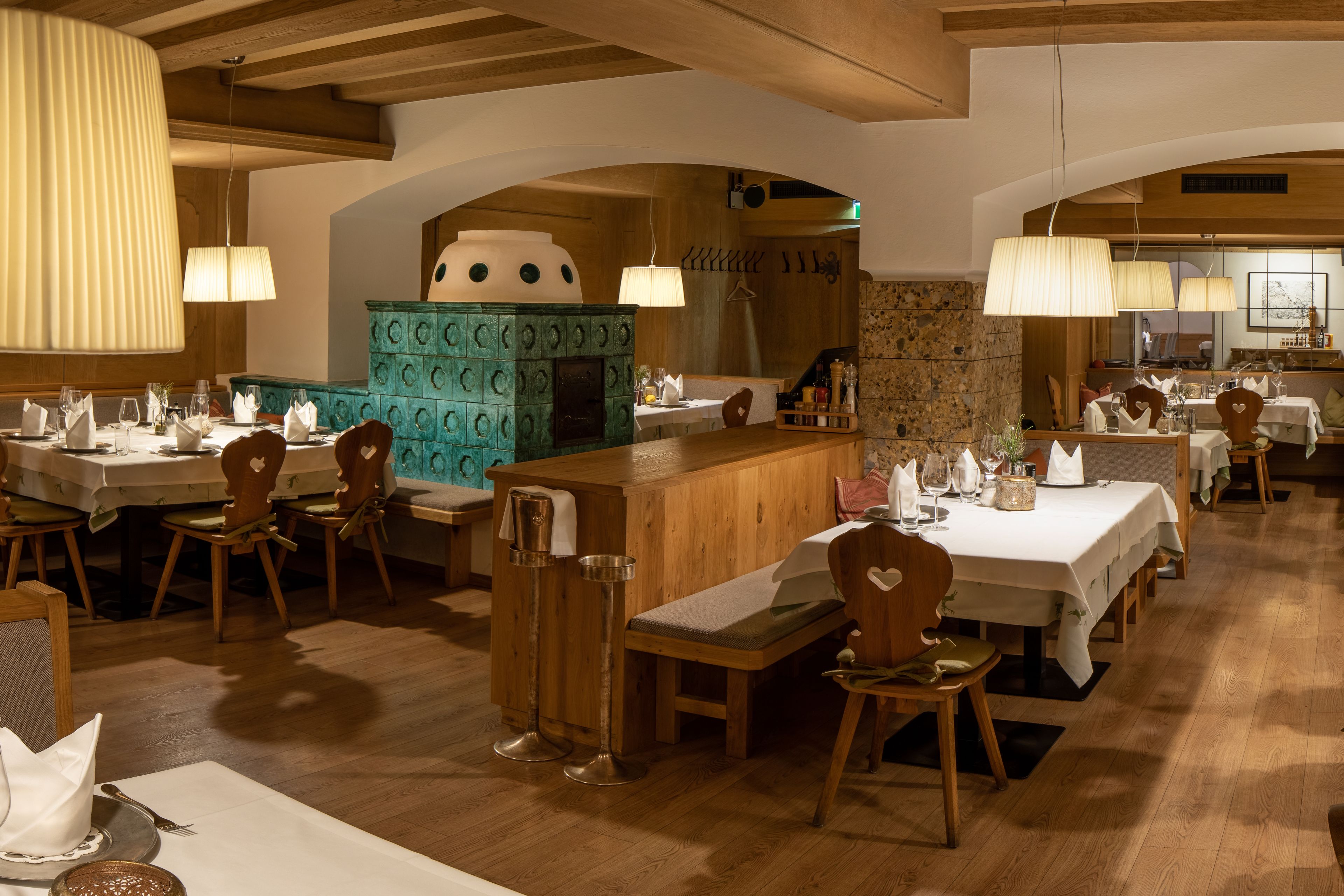 A restaurant with wooden tables and chairs, a central bar area, and pendant lighting.