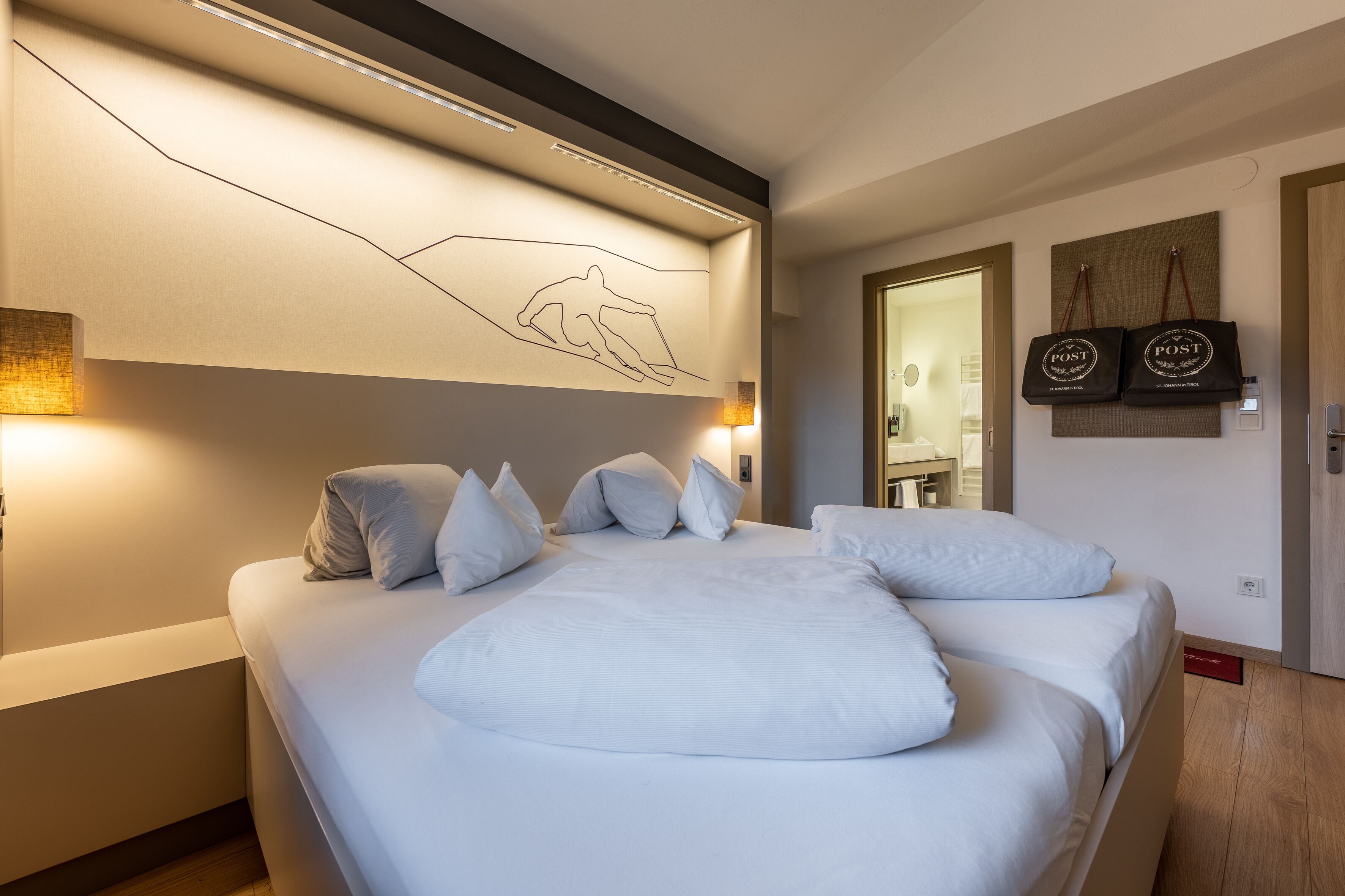 Una habitación de hotel moderna con una cama grande, una obra de arte colgada en la pared y dos bolsos colgados también.