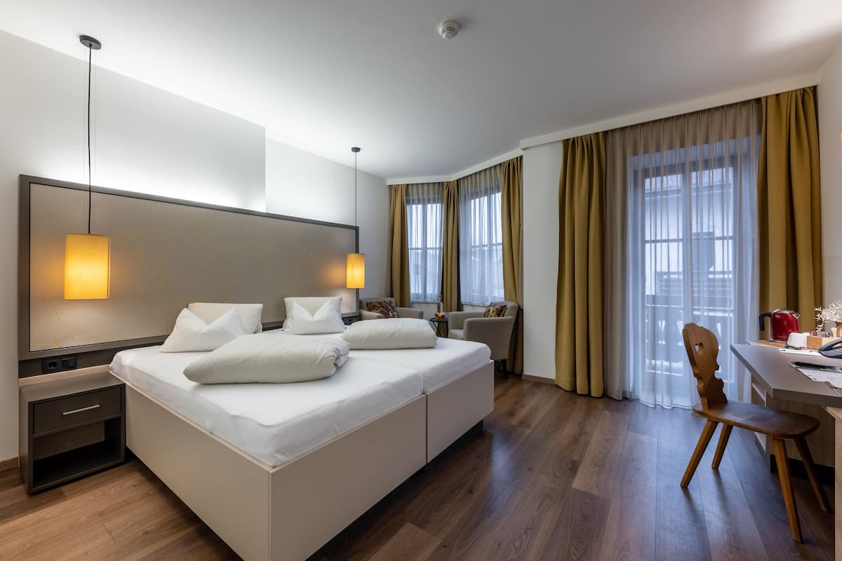 A modern hotel room with a large bed, bedside tables, a desk, and a chair.