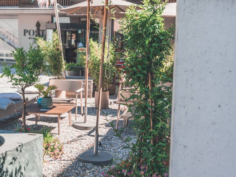 An outdoor seating area with tables and chairs, surrounded by potted plants and a small garden.