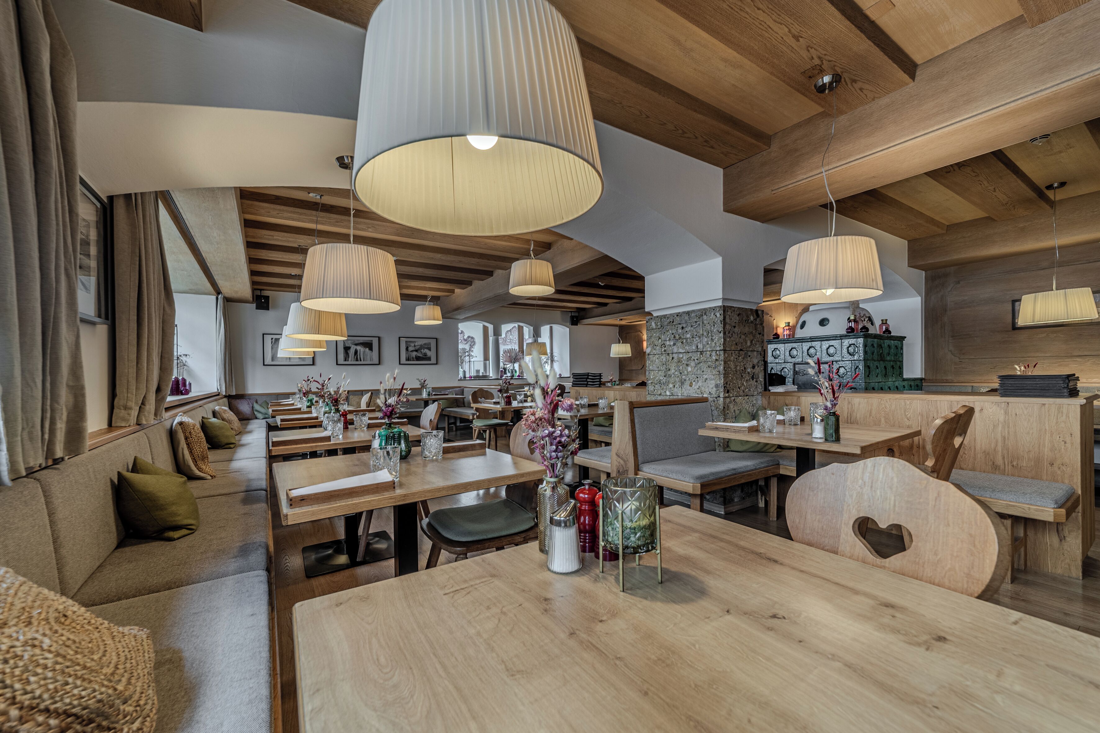 A restaurant with wooden tables and benches, hanging pendant lights, and a kitchen area visible in the background.