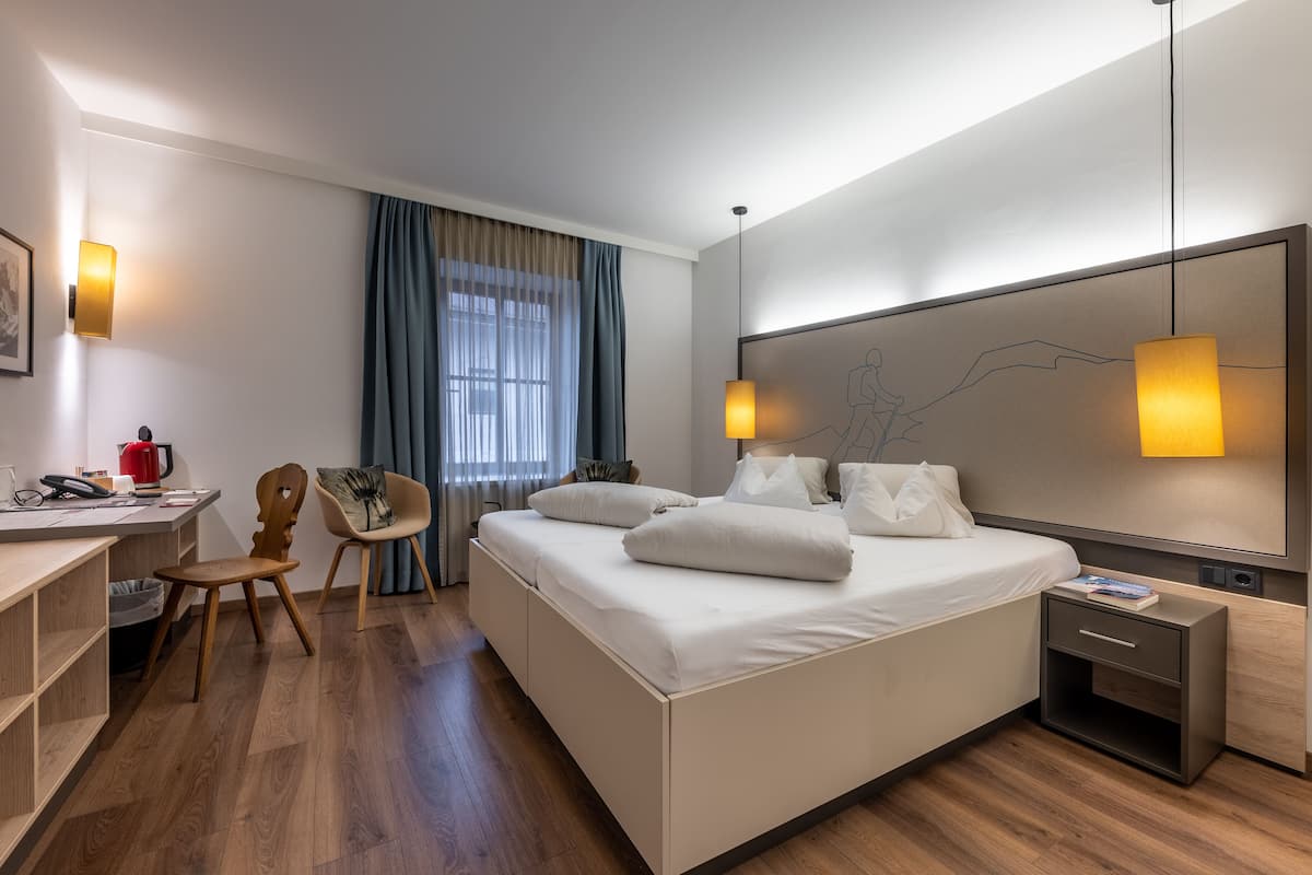A modern hotel room with a large bed, bedside tables, a desk, and a chair.