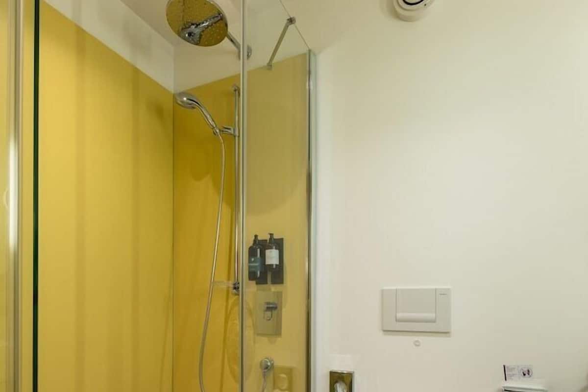 A modern bathroom with a glass shower enclosure, a toilet, and a trash bin.