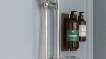 Un baño moderno con ducha de mano, grifo mural y dos botellas de jabón corporal Balsam.