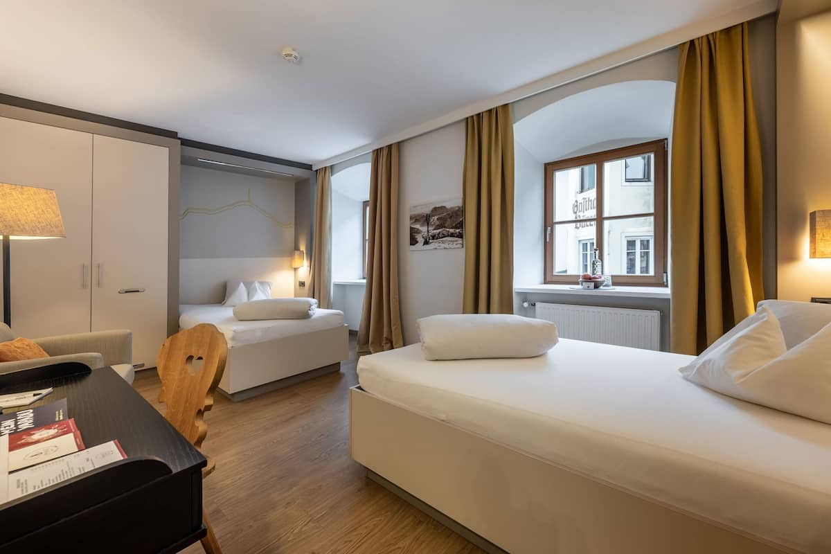 A hotel room with two beds, a desk, a chair, a lamp, and a window with curtains.