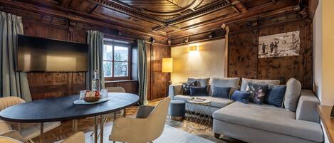 A cozy room with a wooden ceiling, a round dining table with chairs, a sofa, and a TV mounted on the wall.