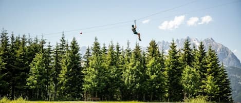 A person zip-lining over a forest with a lake and mountains in the background.