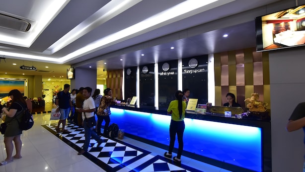 A hotel reception area with a check-in counter, a digital screen displaying room information, and a check-in desk with a receptionist. - Grand Pink Hotel Hat Yai (Hat Yai)