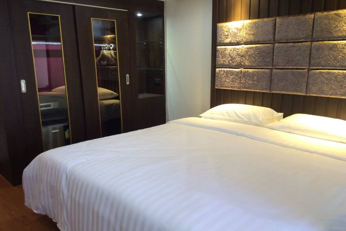 A hotel room with a large bed, a wardrobe with a mirror, and a unique textured wall panel.