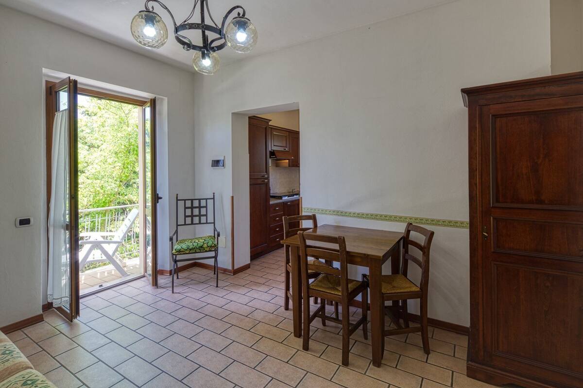 Un coin repas avec une table et des chaises en bois, une cuisine avec des meubles en bois et un balcon doté d’une balustrade.