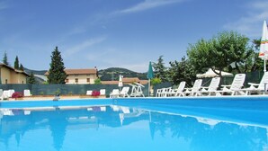 A swimming pool with white lounge chairs and umbrellas, surrounded by greenery and buildings in the background. - Agriturismo Casella del Piano (Gubbio)
