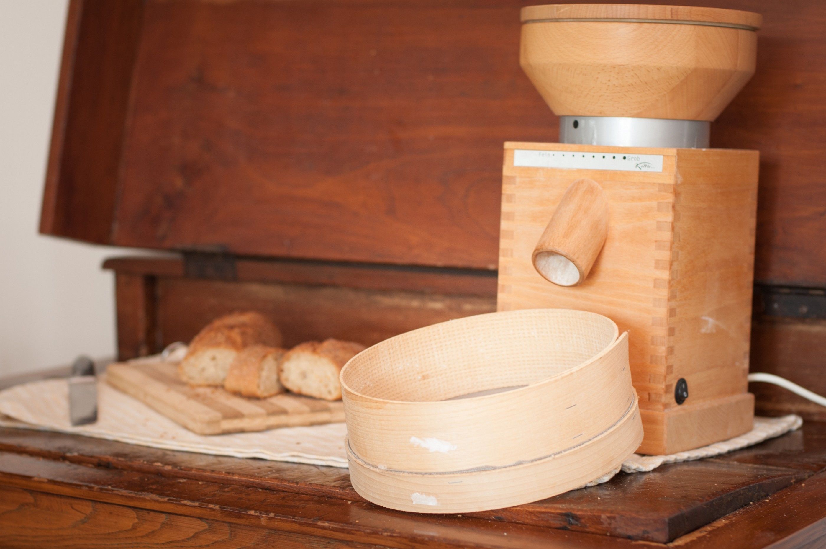 A wooden bread-making machine with a wooden bowl on top and a wooden container beside it.