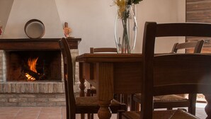 A fireplace with a fire, a wooden table, and chairs in a room with stone walls and a tiled floor. - Agriturismo Casella del Piano (Gubbio)