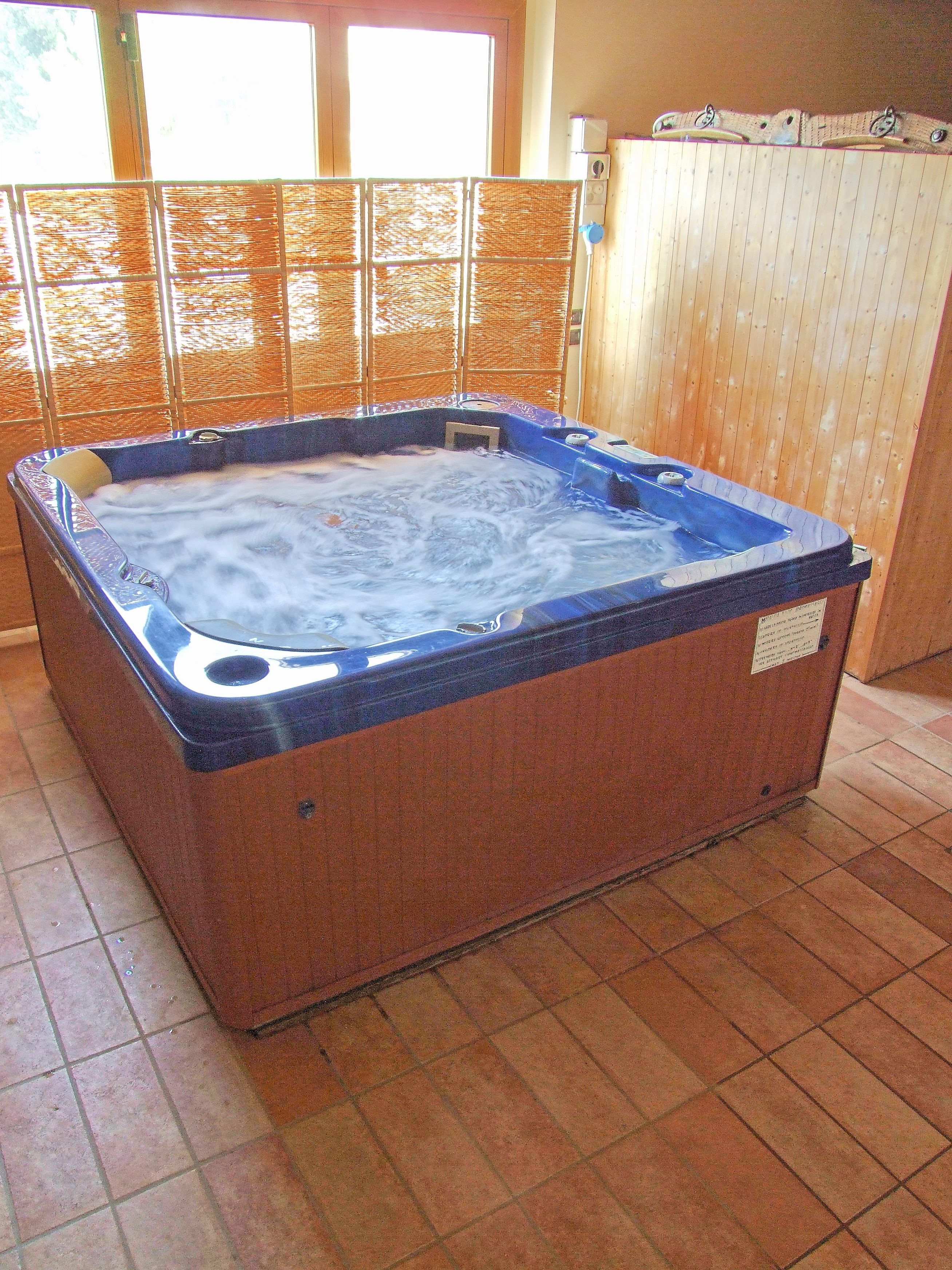 Een hottub met een houten buitenkant en een blauw interieur, gelegen in een ruimte met betegelde vloer en een houten wand.