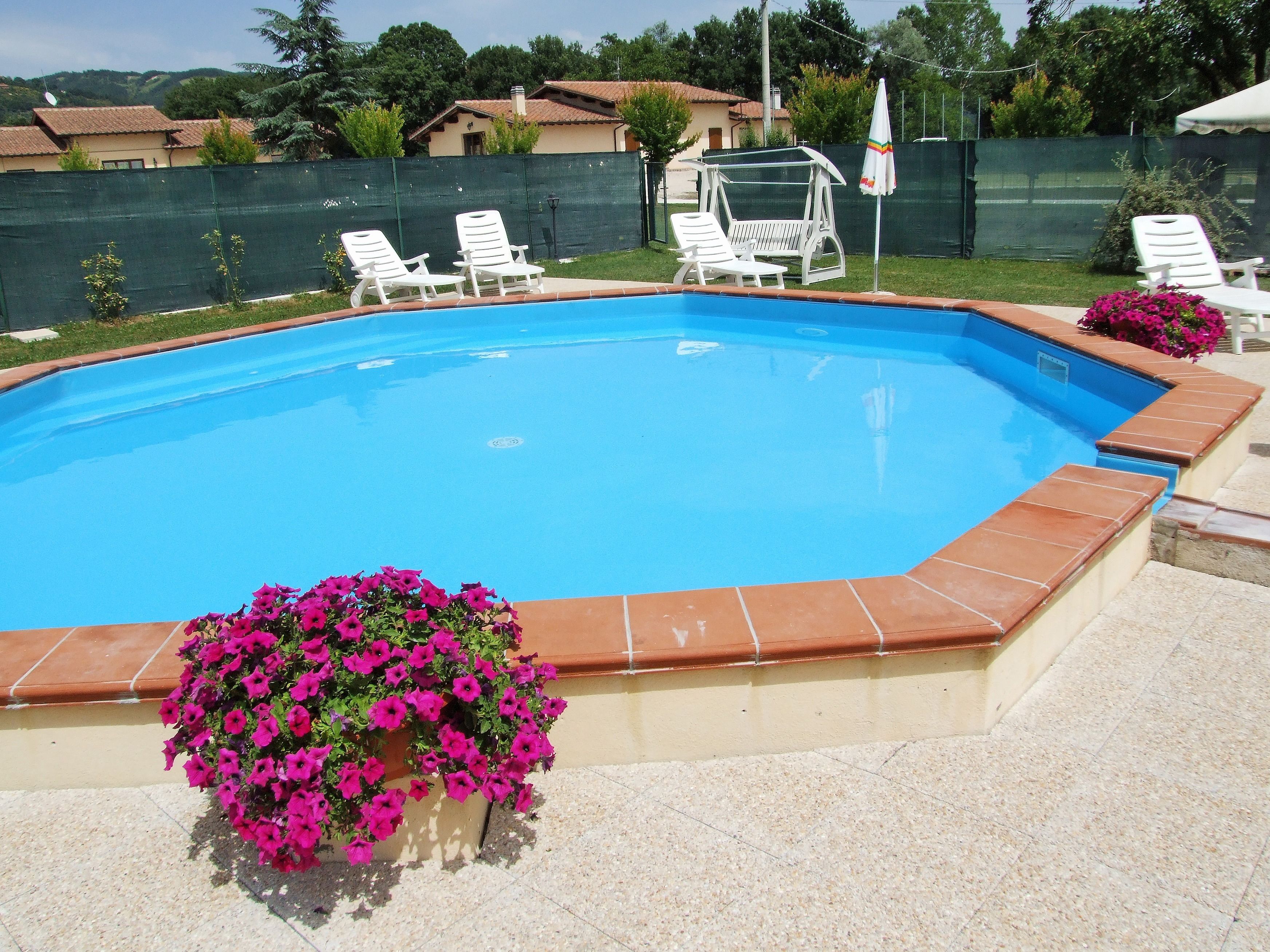 Una piscina con borde de azulejos, rodeada por una cerca y una silla con sombrilla.
