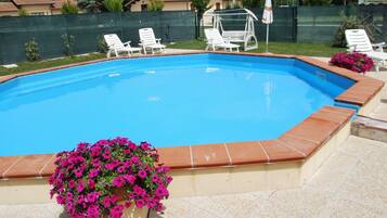 Una piscina con borde de azulejos, rodeada por una cerca y una silla con sombrilla.