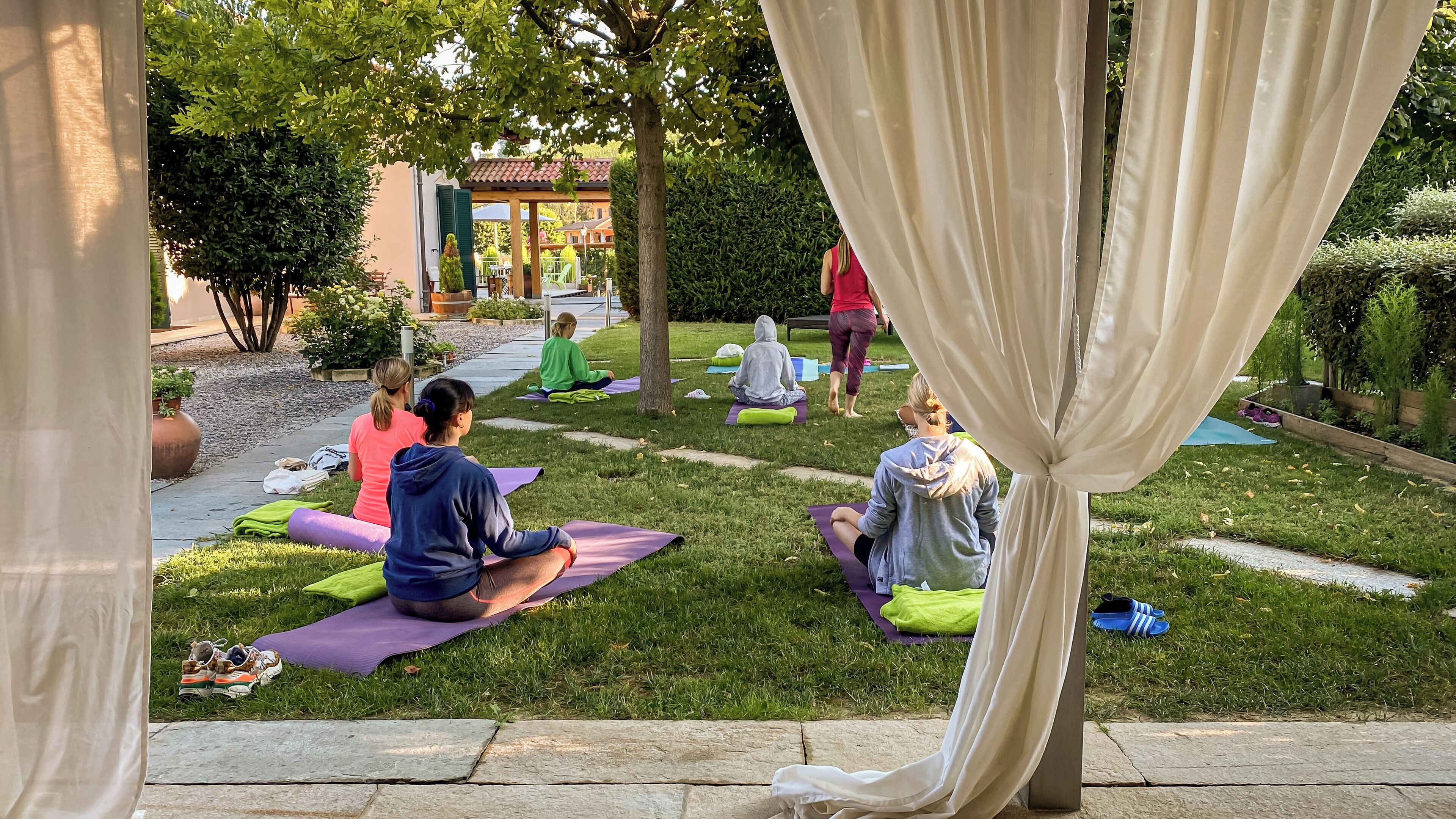 Lezione di yoga all'aperto su un'area erbosa con alberi e un edificio sullo sfondo.