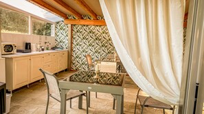 A kitchen with a wooden countertop, a sink, and a microwave. There is a table with chairs and a curtain partially drawn. - La Rosa Gialla (Barolo)
